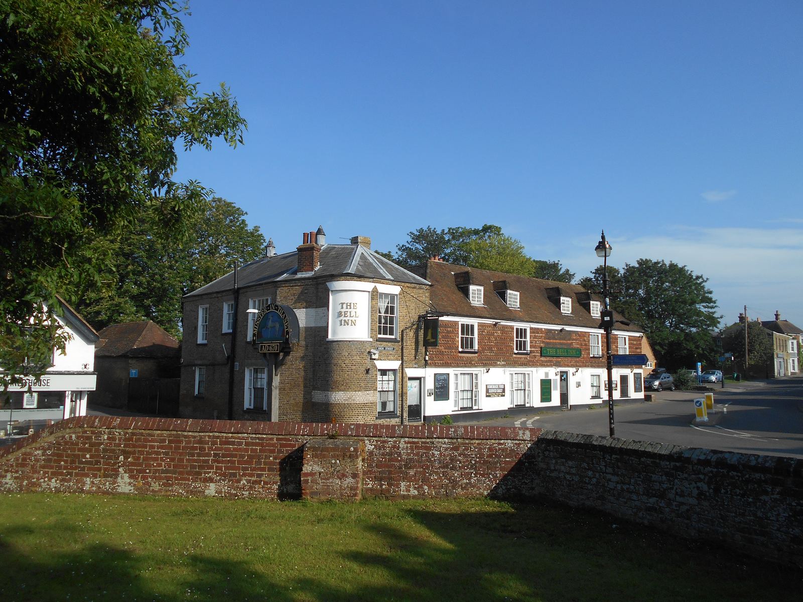 The centre of Minster-in-Thanet village with old brick houses and trees under a blue sky