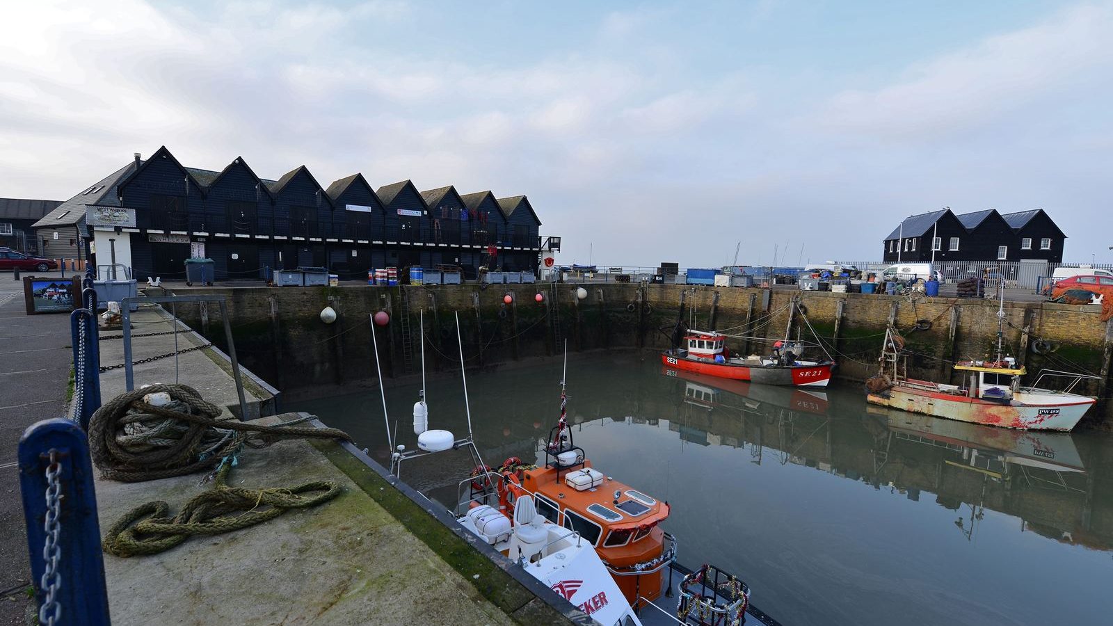 Fishing boats moored in Whitstable harbour beside black weatherboarded sheds